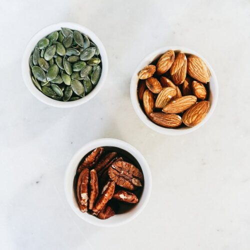 Trei boluri conținând semințe și nuci diverse pe o masă albă - alimentele sunt bogate în Omega-3