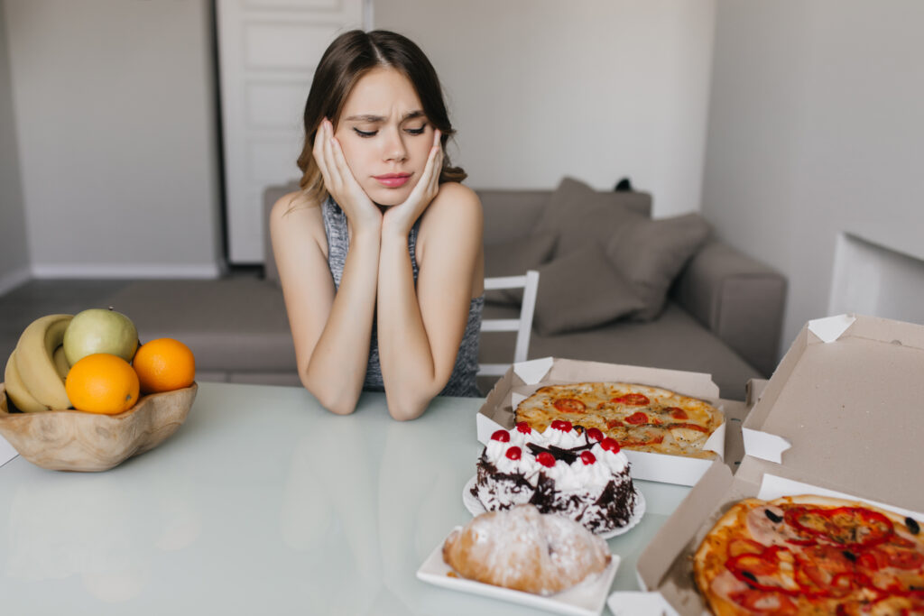 femeie la dieta care se uita la mancare nesanatosa, suparata