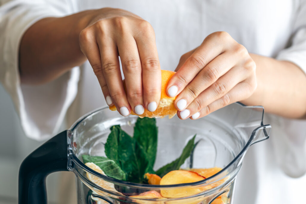 Femeie care stoarce o portocala intr-un smoothie de slaăbit pentru detoxifiere, imagine de aproape