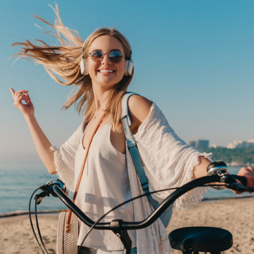 Fata tanara blonda, zambeste catre camera, stand langa o bicicleta pe plaja