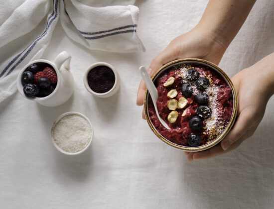 Imagine de sus cu mâinile unei persoane care ține un bol cu desert de dietă: smoothie bowl cu iaurt, fructe de pădure, fulgi de cocos
