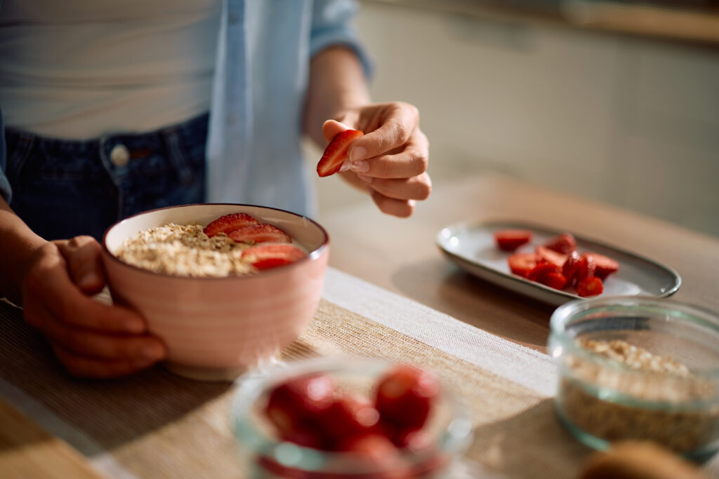 Imagine de aproape, femeie tânără care pregătește terci de ovăz cu căpșuni, un preparat integral recomandat în dieta Ornish