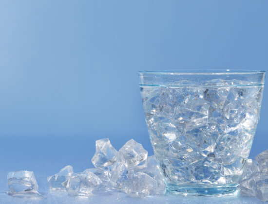 un pahar de apa plin cu cuburi de gheata, cuburi de gheata pe langa pahar, fundal albastru