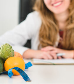 tanara fericita care sta la masa, portii de fructe si legume cantarite