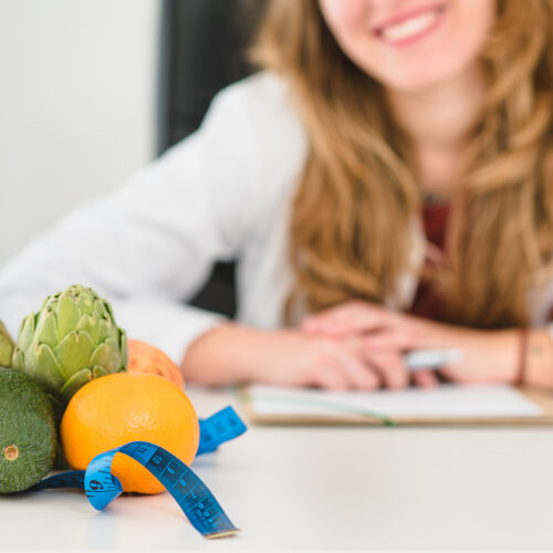 tanara fericita care sta la masa, portii de fructe si legume cantarite