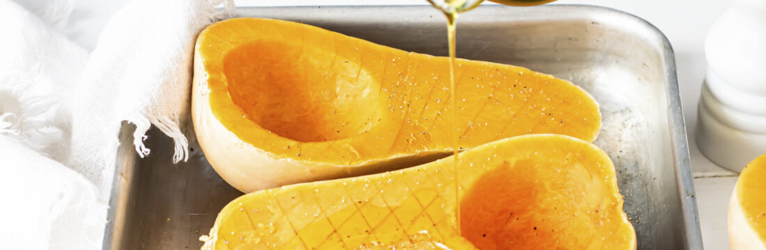 bucati de dovleac taiate pe jumatate pe tava, mana unei femei adauga peste ulei de măsline