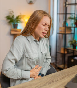 Femeie cu dureri de stomac, posibil efect advers al administrării suplimentelor cu berberină. Imagine la birou