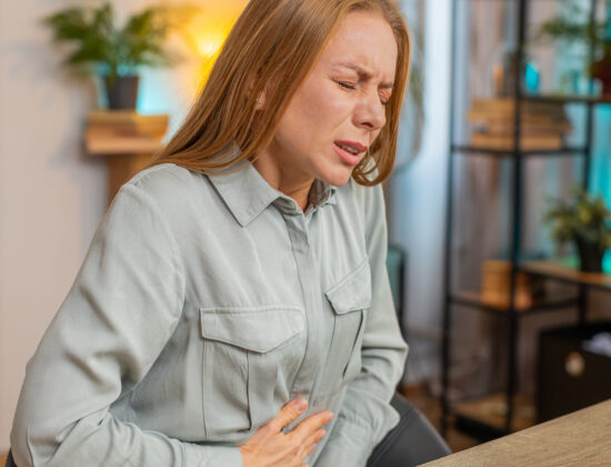 Femeie cu dureri de stomac, posibil efect advers al administrării suplimentelor cu berberină. Imagine la birou