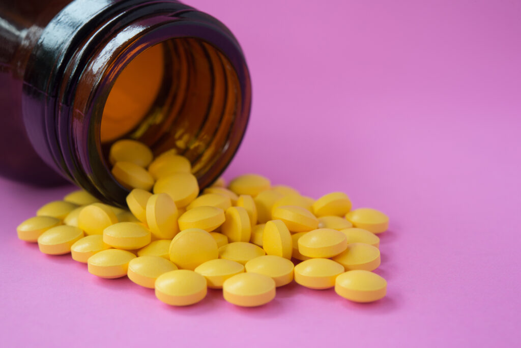 Berberină în format de supliment. Pastile galbene care se revarsă dintr-un flacon, pe un fundal mov. Imagine de aproape