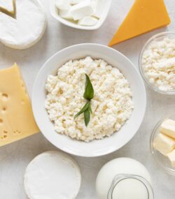 Imagine de sus cu diferite sortimente de lactate. In centru, un bol alb cu cottage cheese, aliment bogat în proteine, optim într-o dietă de slăbit