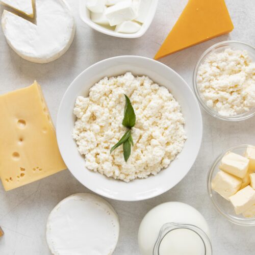 Imagine de sus cu diferite sortimente de lactate. In centru, un bol alb cu cottage cheese, aliment bogat în proteine, optim într-o dietă de slăbit