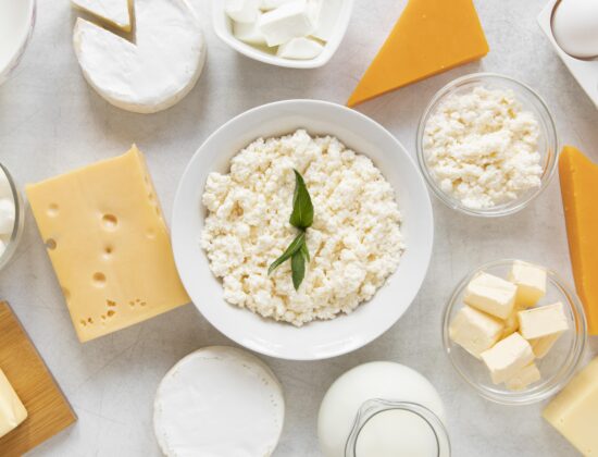 Imagine de sus cu diferite sortimente de lactate. In centru, un bol alb cu cottage cheese, aliment bogat în proteine, optim într-o dietă de slăbit