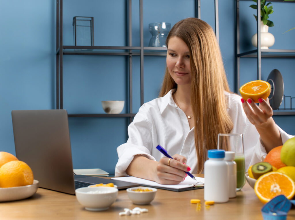 Medic nutriționist tănăr, are un consult online. Pe birou, se observă fructe proaspete și borcănele cu suplimente recomandate într-o dietă hipocalorică.