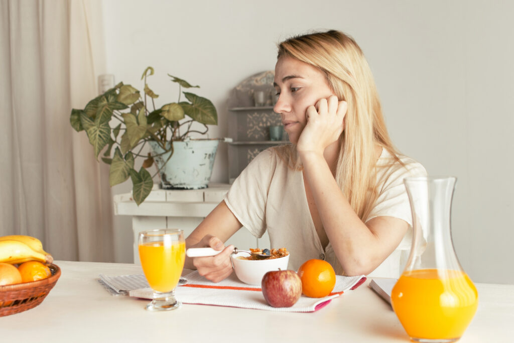 Fată tânără, ia micul dejun la masă. Resimte oboseala, în ciuda alimentelor sanatoase alese, efect secundar într-o dietă alcalină