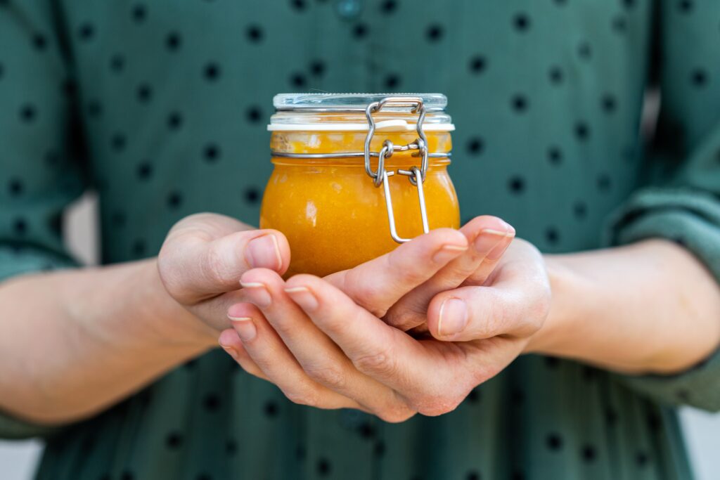 Imagine de aproape, persoană care ține în plame un borcănel transparent de dulceața de gutui, rețetă fără zahăr