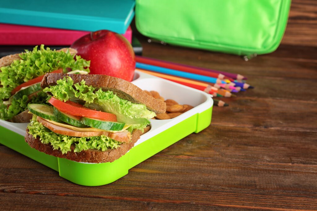 Imagine de aproape, sandwich cu pâine integrală și legume proaspete, într-o cutiuță de prânz, lângă un măr și migdale