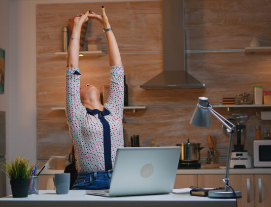 Femeie tânără face exerciții de întindere la birou, pentru ași crește nivelul de mișcare zilnică