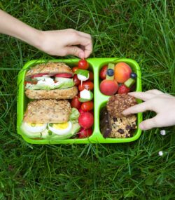 Imagine de sus, pacheețe sănătos penrtu școală așezat pe iarbă. Conține alimente integrale, potrivite pentru copii aflați în creștere.