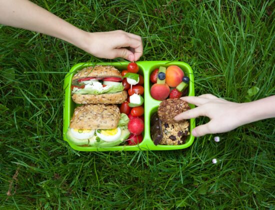 Imagine de sus, pacheețe sănătos penrtu școală așezat pe iarbă. Conține alimente integrale, potrivite pentru copii aflați în creștere.