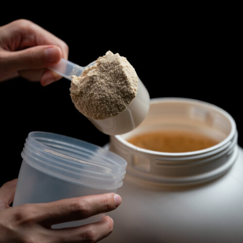 Imagine de aproape, mâna unei persoane care scoate dintr-un recipient mare o cupă de creatină pudră