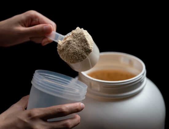 Imagine de aproape, mâna unei persoane care scoate dintr-un recipient mare o cupă de creatină pudră