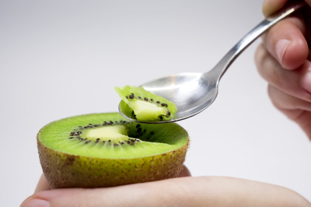 Persoană care mănâncă o jumătate de kiwi cu lingurița. Imagine de aproape