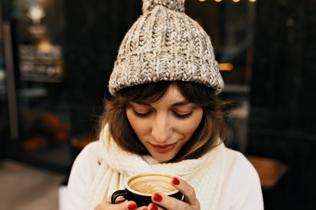 Imagine de aproape, femeie îmbrăcată gros, ține în mâini o cană de pumpkin spice latte