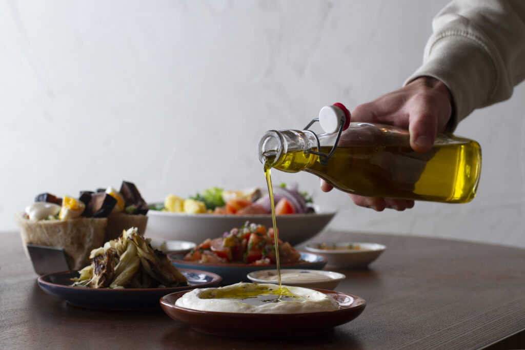Imagine de aproape, persoană care toarnă ulei de măsline peste hummus