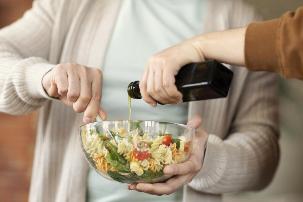 Persoană care toarnă ulei de masline extravirgin presat la rece peste un bol de salată caldă de paste