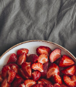 Imagine de sus, ceașcă de cafea, bol cu căpșuni și un ceas pe un cearceaf gri