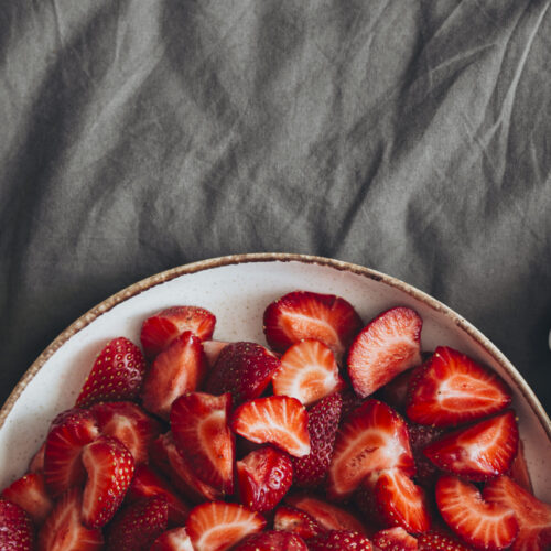 Imagine de sus, ceașcă de cafea, bol cu căpșuni și un ceas pe un cearceaf gri