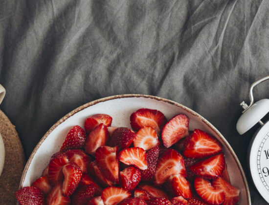 Imagine de sus, ceașcă de cafea, bol cu căpșuni și un ceas pe un cearceaf gri