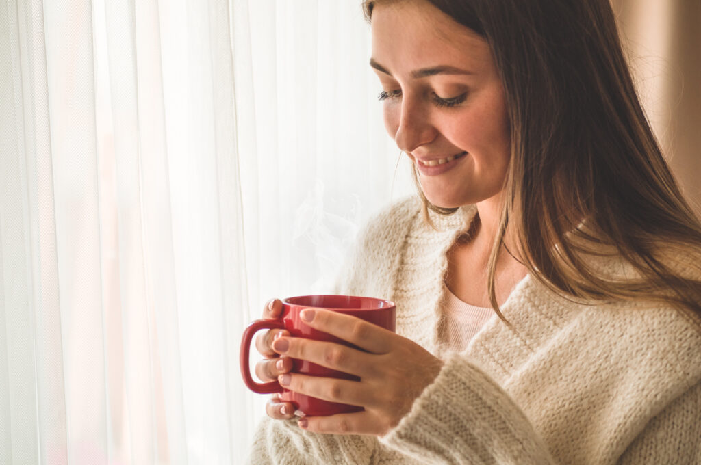 Imagine de aproape, femeie care zâmbește ține o cană roșie cu ceai în mâini
