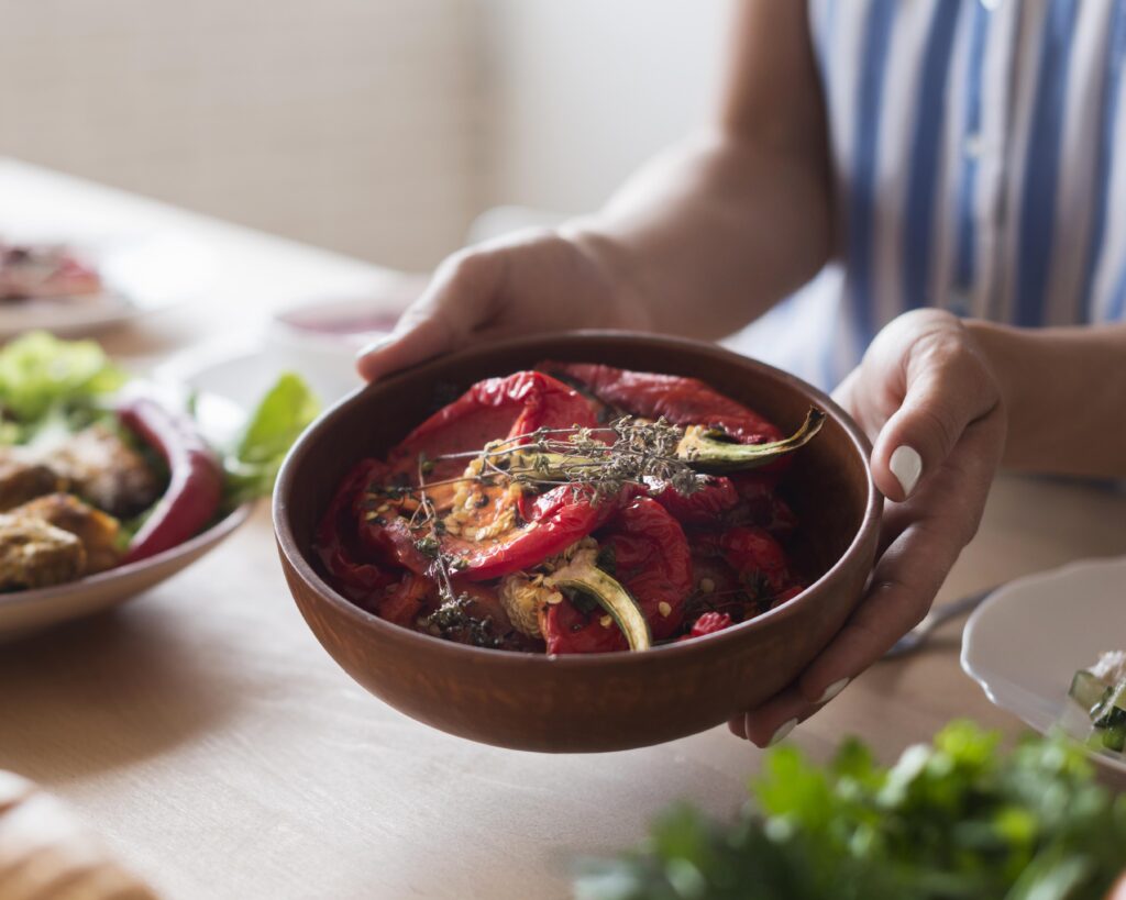 Imagine de aproape, salată de ardei copți într-un bol de bambus pe care îl ține o persoană