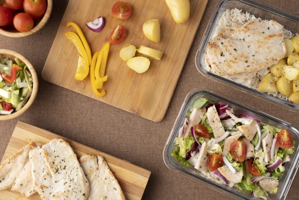 Imagine de sus, alimente permise în dieta nordică, așezate în caserole. Câteva legume proaspete tăiate pe un tocător de lemn