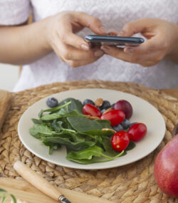 femeie sta la masa cu o salata sanatoasa in fata, tine in mana telefonul