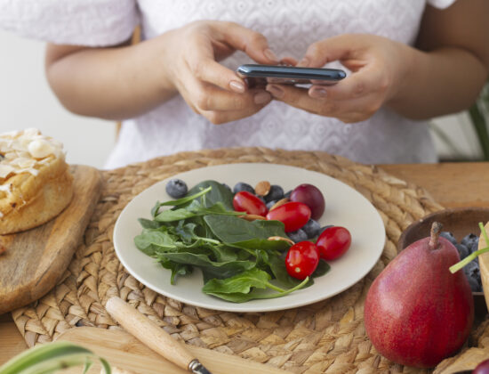 femeie sta la masa cu o salata sanatoasa in fata, tine in mana telefonul