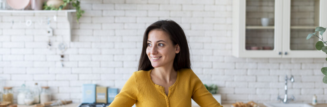 femeie in bucatarie fericita, multumita, zambeste