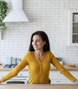 femeie in bucatarie fericita, multumita, zambeste