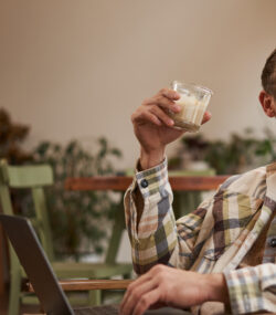 un barbat bea o bautura de craciun langa brad si sta la laptop