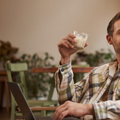 un barbat bea o bautura de craciun langa brad si sta la laptop