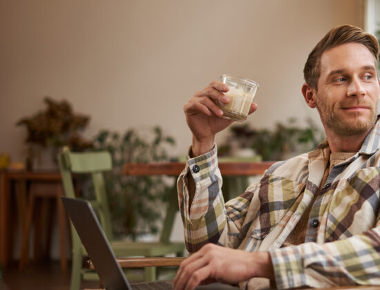 un barbat bea o bautura de craciun langa brad si sta la laptop
