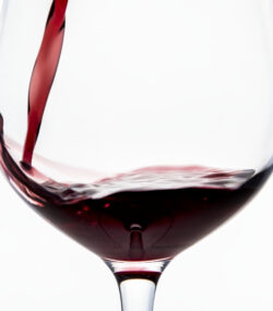 vin rosu turnat in pahar de vin pe fundal alb